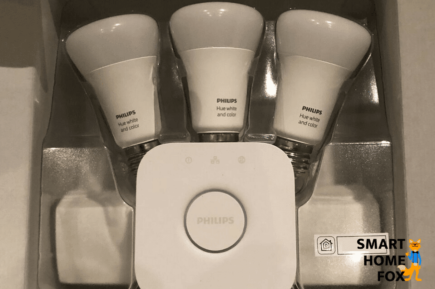 Man sieht eine Philips Hue Bridge mit Hue Leuchtelementen im Hintergrund.